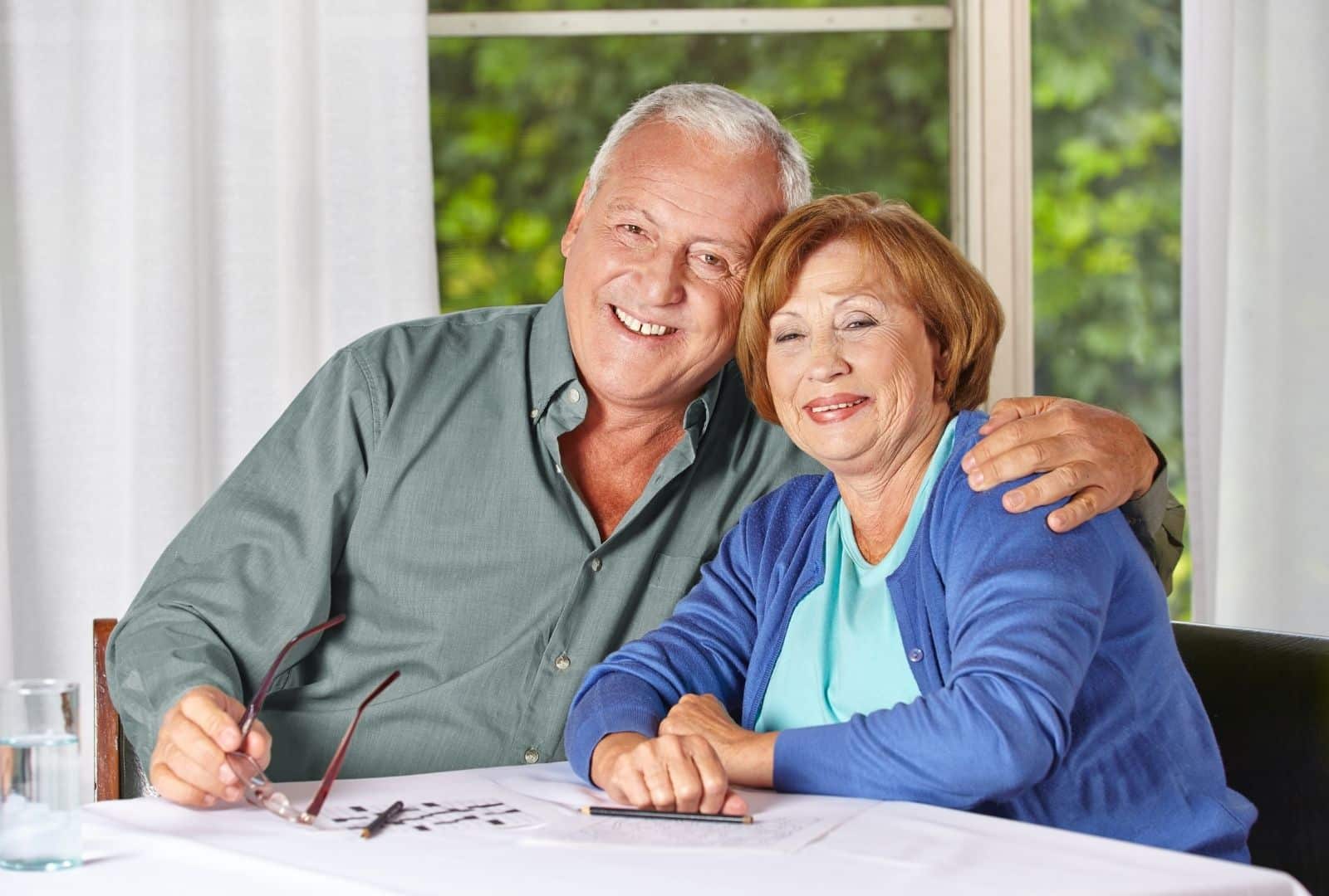 זוג קשישים מחבקים זה את זה בחמימות על ספה בסלון ביתי, מסמל תמיכה משפחתית לניידות נוחה יותר עם תו נכה לרכב.