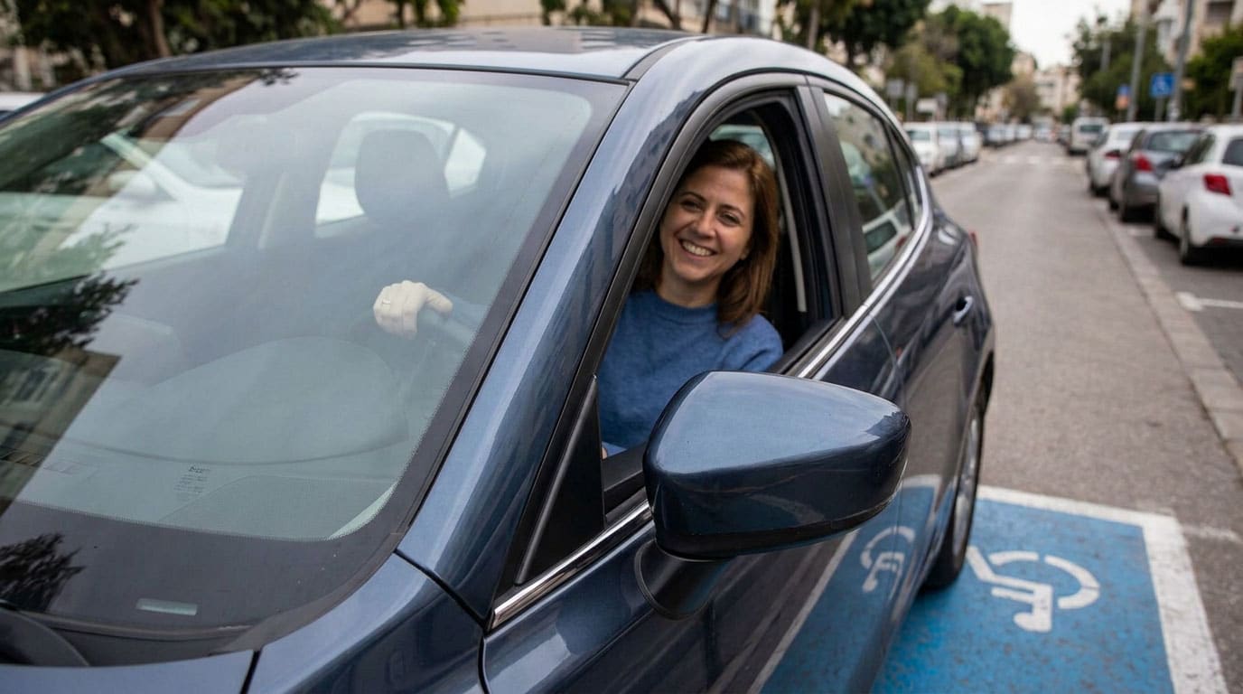 צילום מקרוב של אישה מחייכת היושבת בתוך מכונית כחולה, כשידה על ההגה. מחוץ למכונית, על גבי הכביש, נראה סימון כחול של חניית נכה עם סמל כיסא גלגלים בלבן. המכונית חונה בתוך תחום הסימון ברחוב עירוני.